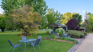 A covered outdoor seating area with a table and chairs, surrounded by well-maintained grass and trees. - Beechworth Motor Inn (Beechworth)