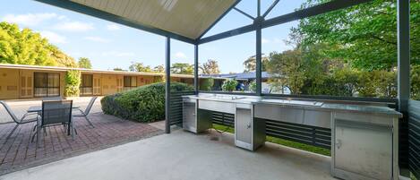 An outdoor kitchen area with a concrete floor, a metal counter, and a glass enclosure.