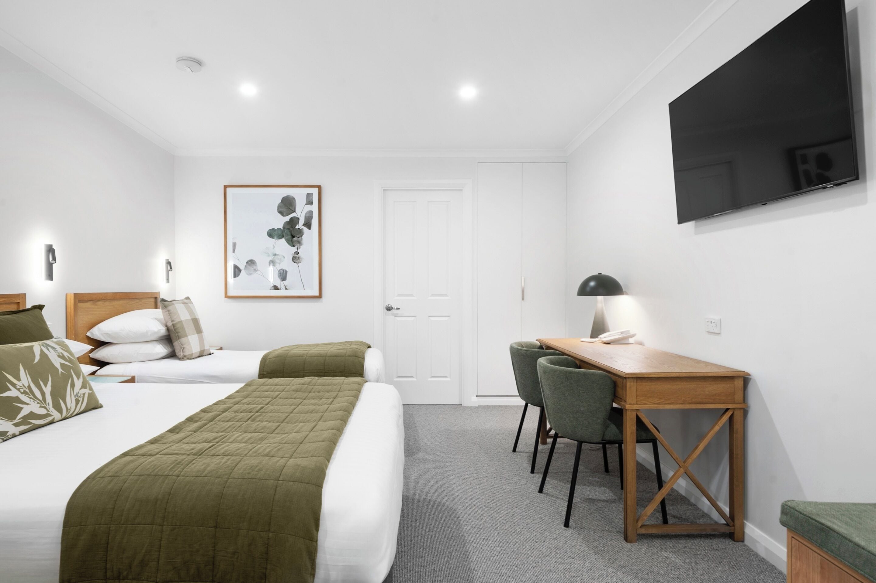 Habitación de hotel con dos camas, un escritorio con sillas, un televisor de pantalla plana y una obra de arte enmarcada en la pared.