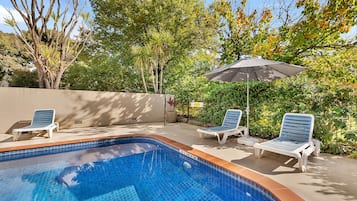 Una piscina al aire libre, sombrillas, sillones reclinables de piscina