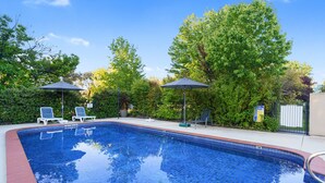 A swimming pool with blue tiles, surrounded by greenery and two umbrellas. - Beechworth Motor Inn (Beechworth)