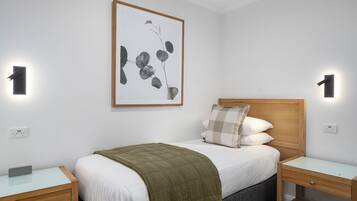 A neatly arranged bedroom with a bed, two bedside tables, a wall-mounted light, and a framed artwork.