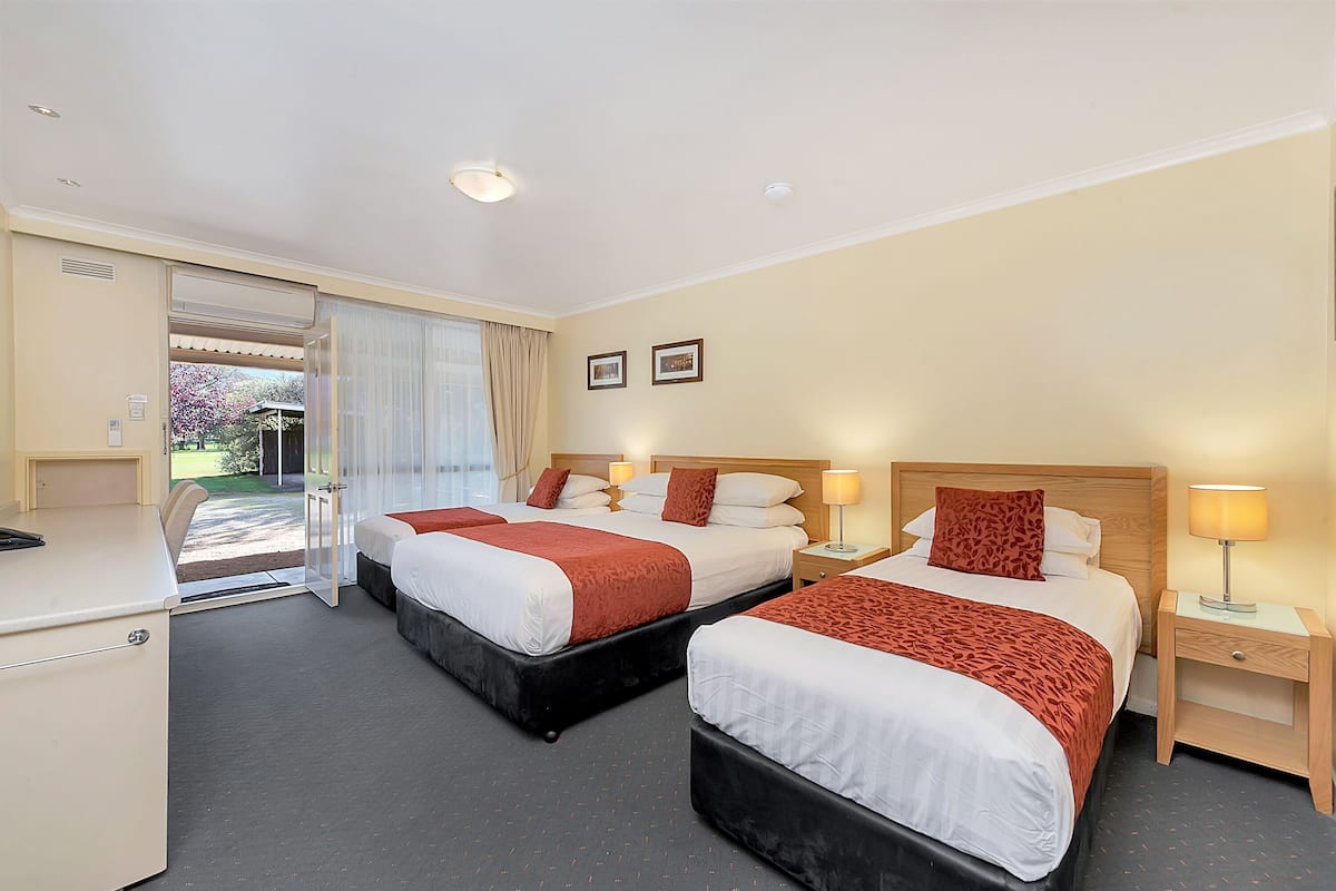 A hotel room with two beds, a desk, and a view of the outdoors.
