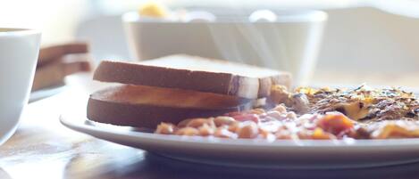 A plate of food with toast and beans, a white cup, and a white bowl in the background.