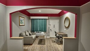 A living room with a grey sofa, a coffee table, a desk with a chair, a door, and a mirror. - Hotel Bliss Kemah (Kemah)