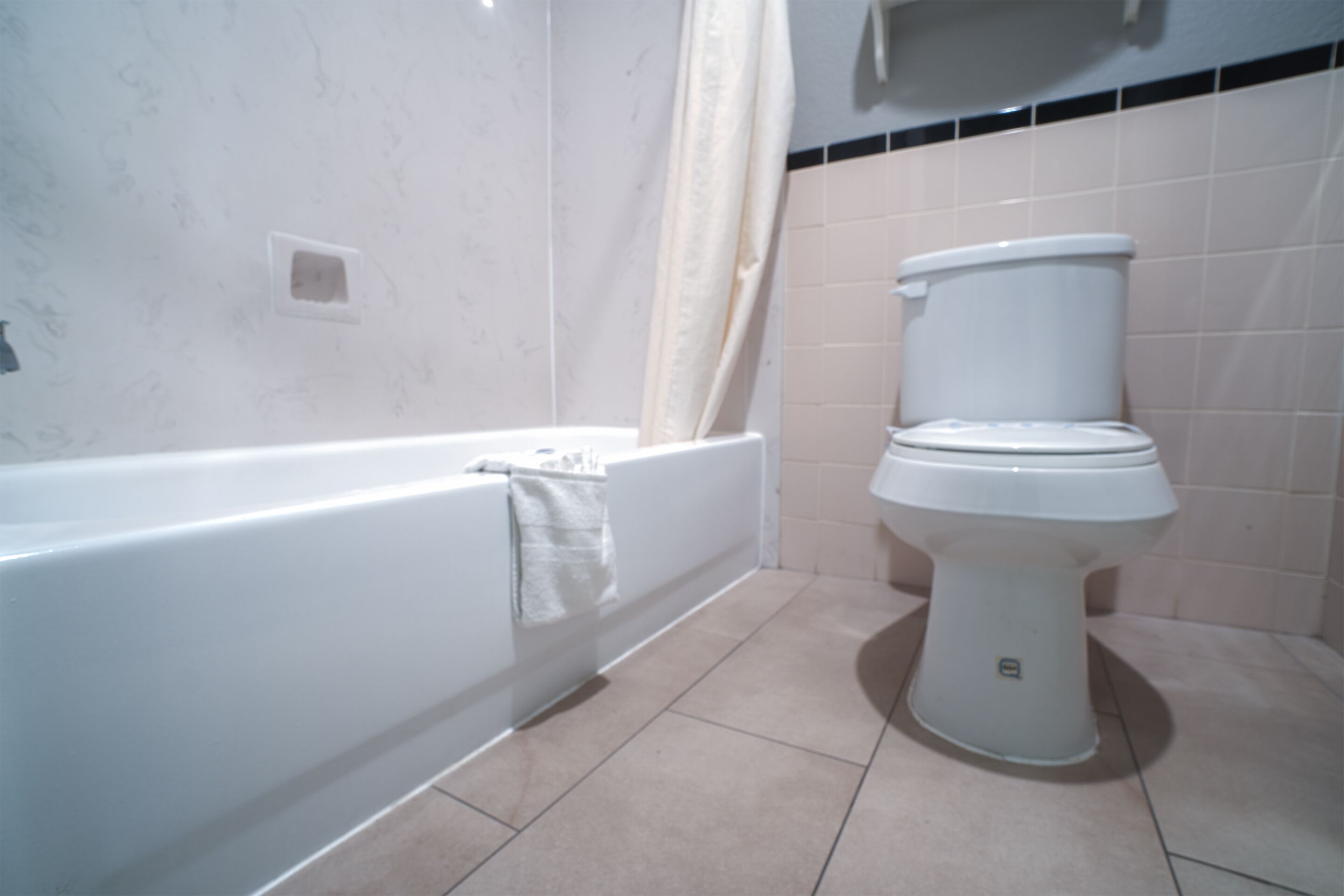 A bathroom with a white bathtub, a toilet, and beige tiled walls.