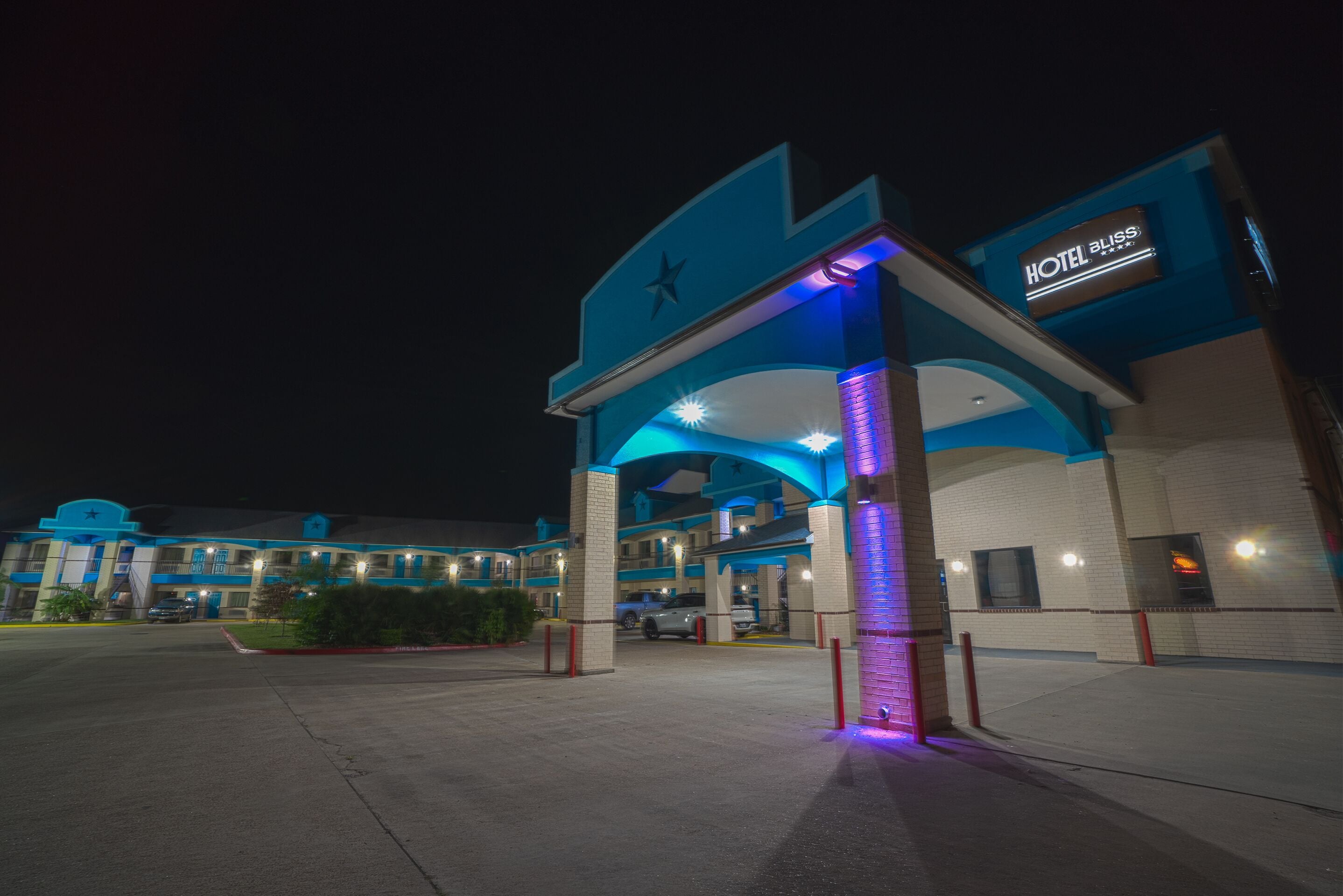 A hotel entrance with a star logo, a sign indicating it is a hotel, and a parking lot with a few cars.