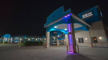 A hotel entrance with a star logo, a sign indicating it is a hotel, and a parking lot with a few cars.