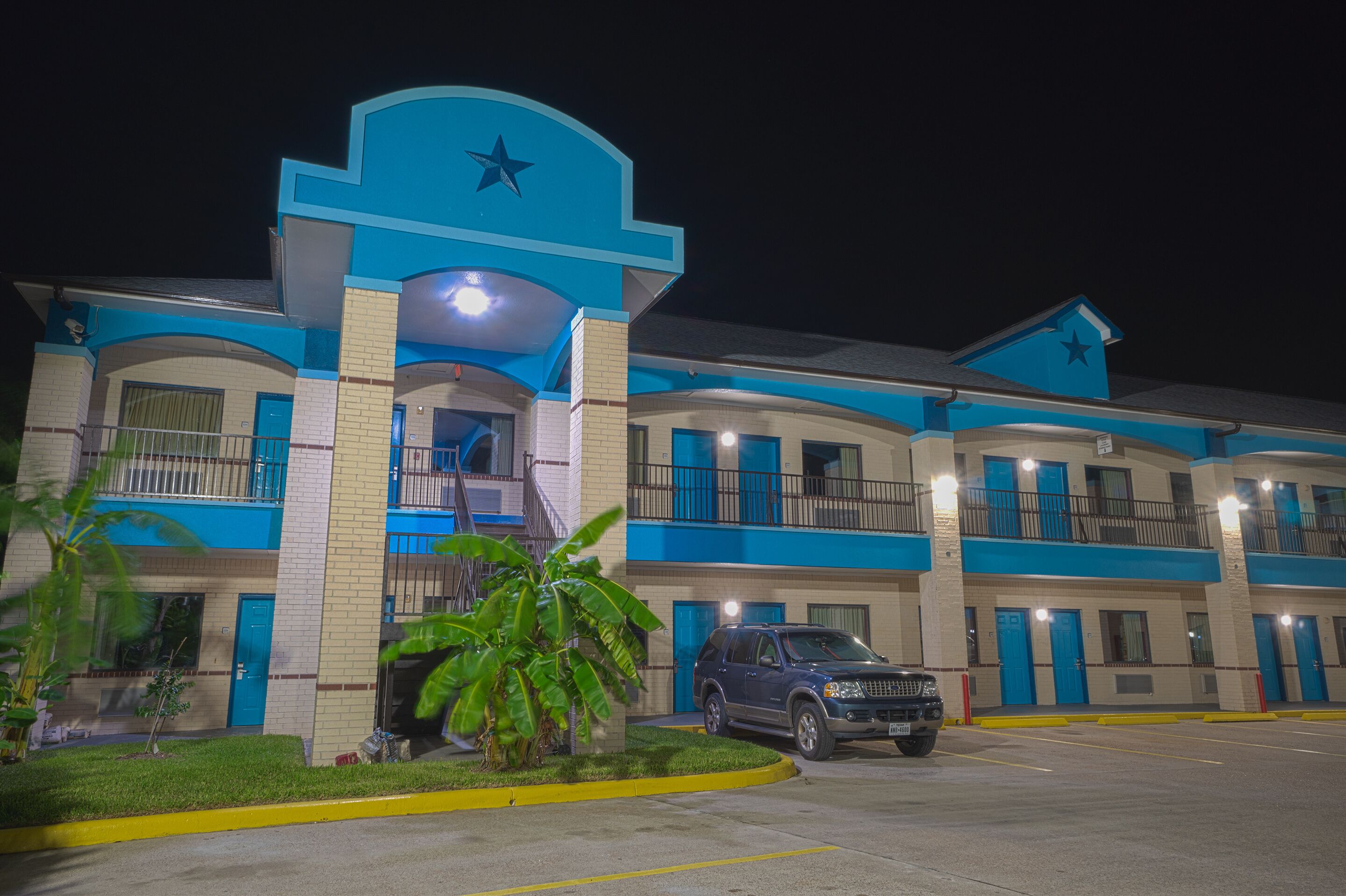 A multi-story hotel with a blue and white color scheme, featuring balconies and a parking area.