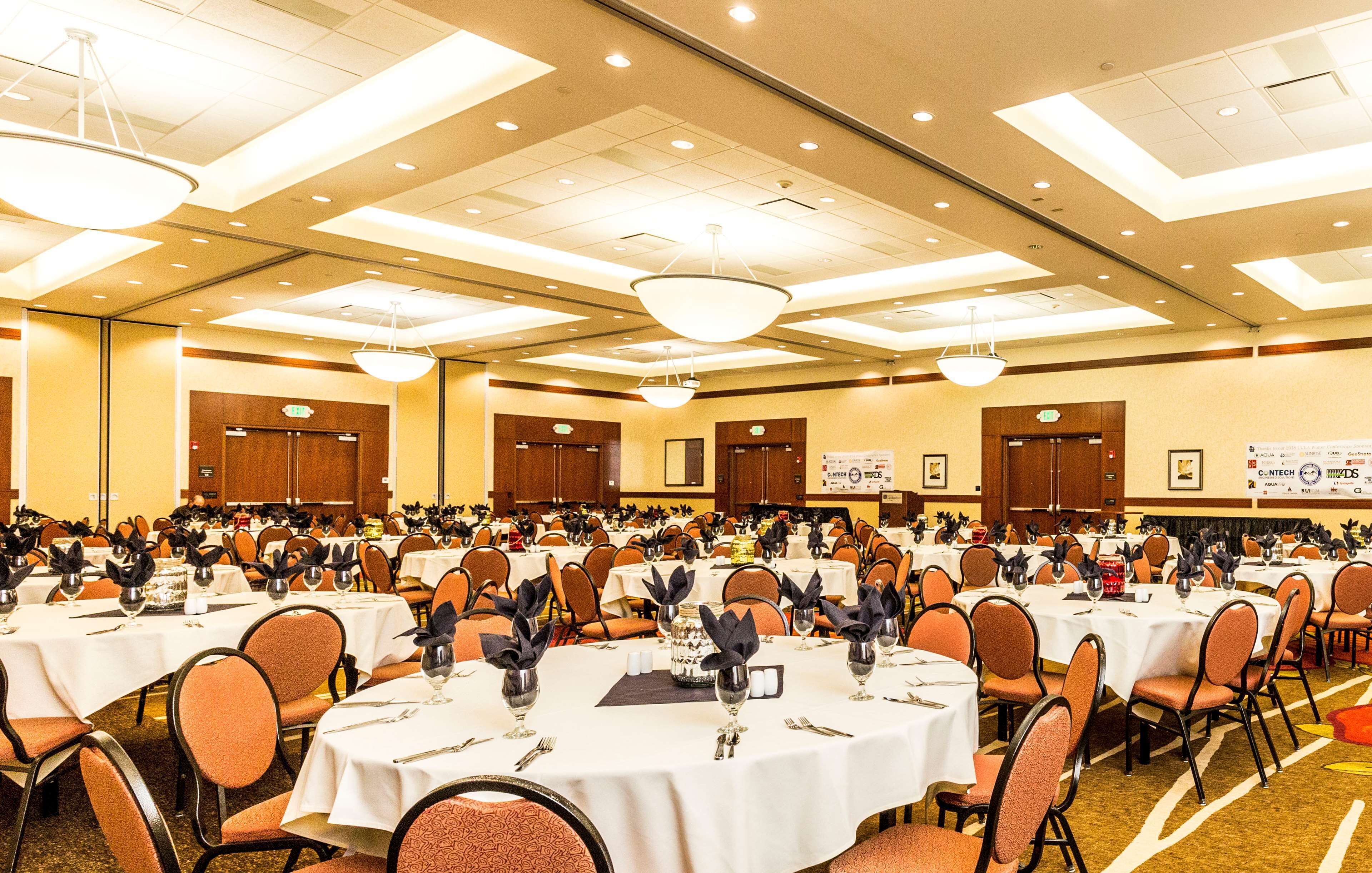 Un amplio salón de banquetes con varias mesas redondas dispuestas para comidas, equipado con sillas y cubiertos.