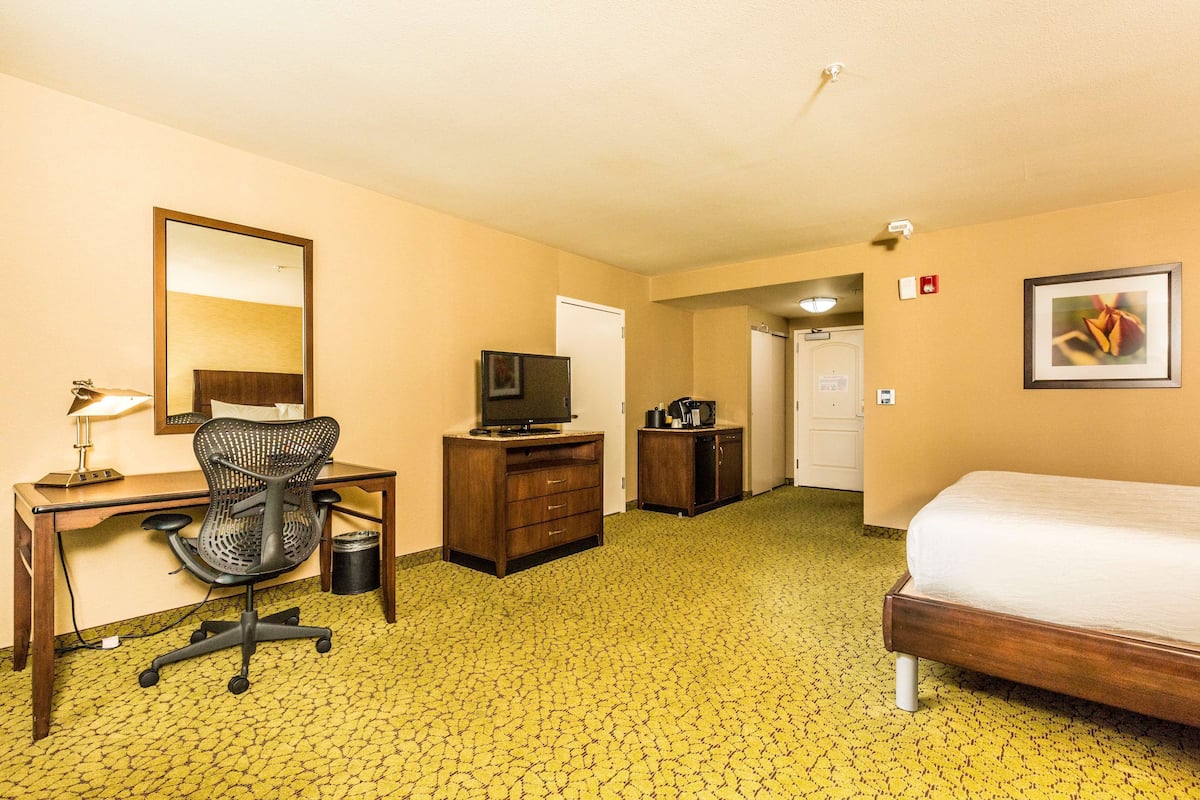 A hotel room with a bed, desk, chair, television, and a small kitchenette.