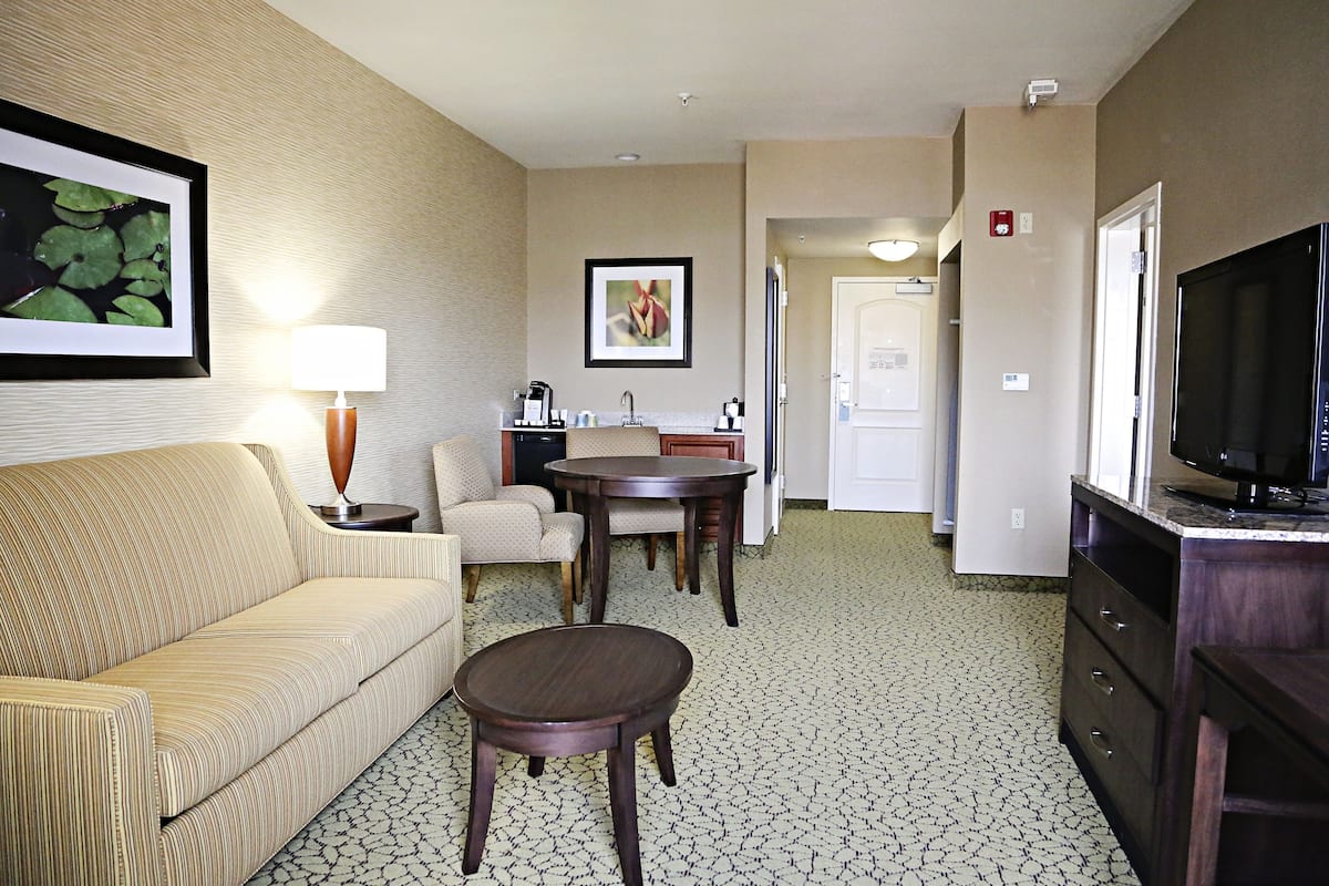 A hotel room with a sofa, a small round table, a chair, a television, and a kitchenette area.