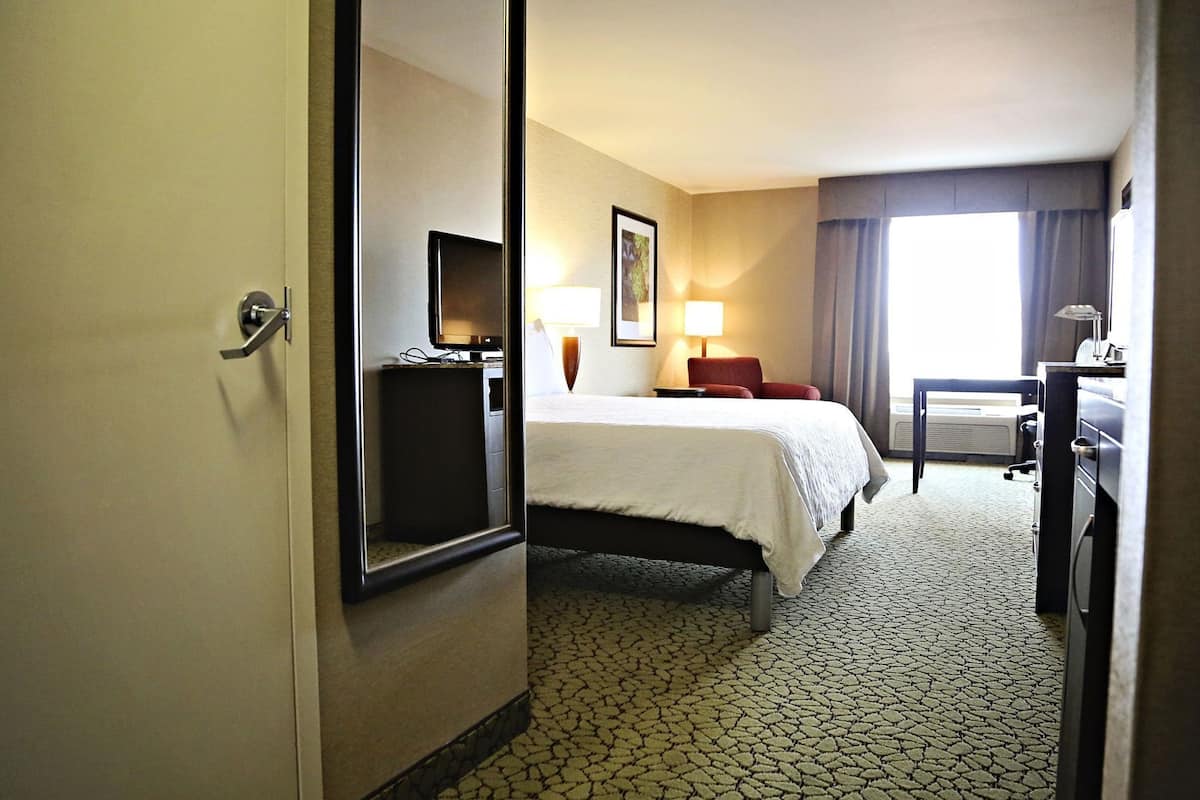 A hotel room with a bed, a desk, a chair, a TV, and a lamp.