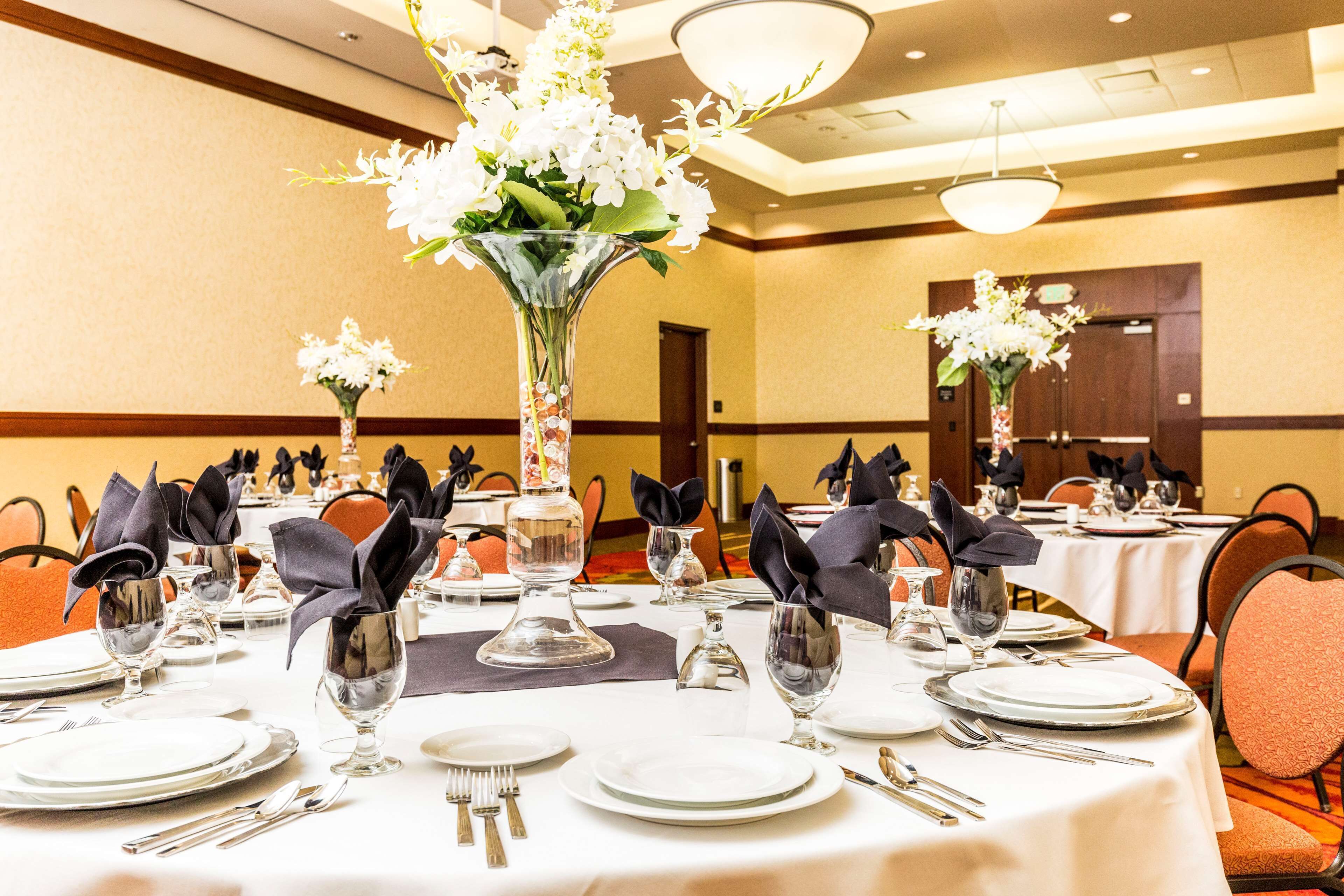 A banquet hall with round tables set for dining, each with white tablecloths, silverware, and dark napkins.