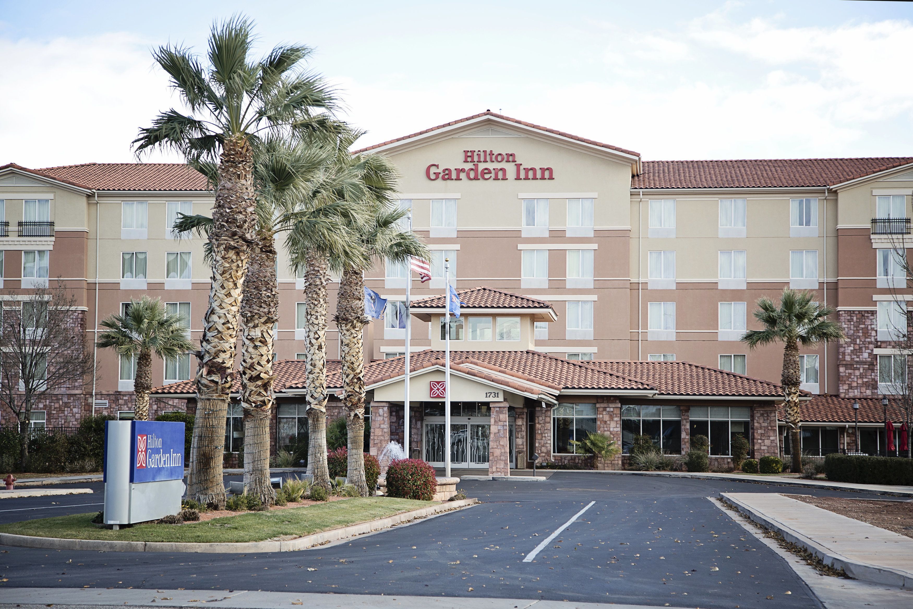 A Hilton Garden Inn with a brick facade, multiple windows, and palm trees in the foreground.