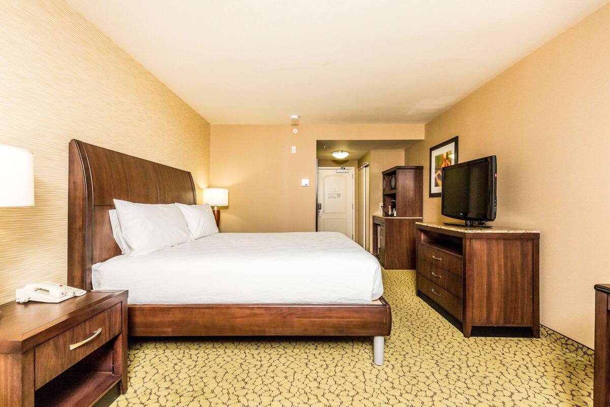 A hotel room with a bed, bedside table, lamp, TV, and a wardrobe.
