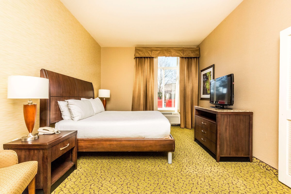 A hotel room with a large bed, bedside lamps, a desk with a telephone, a television, and a window with curtains.