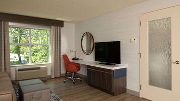 A modern hotel room with a large window, a desk with a flat-screen TV, a red office chair, and a wooden cabinet.