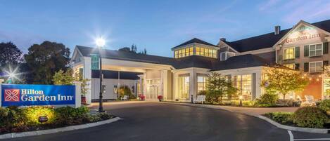 Un Hilton Garden Inn con una entrada bien iluminada, un cartel y un área de estacionamiento.