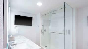 Un baño moderno con ducha envuelta en vidrio, lavamanos de mármol y televisor montado en la pared.