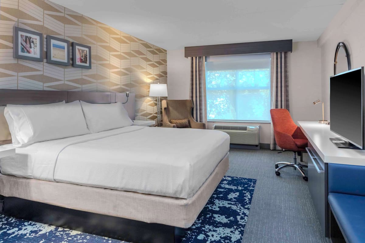 A hotel room with a large bed, a desk with a chair, a TV, and a window with curtains.