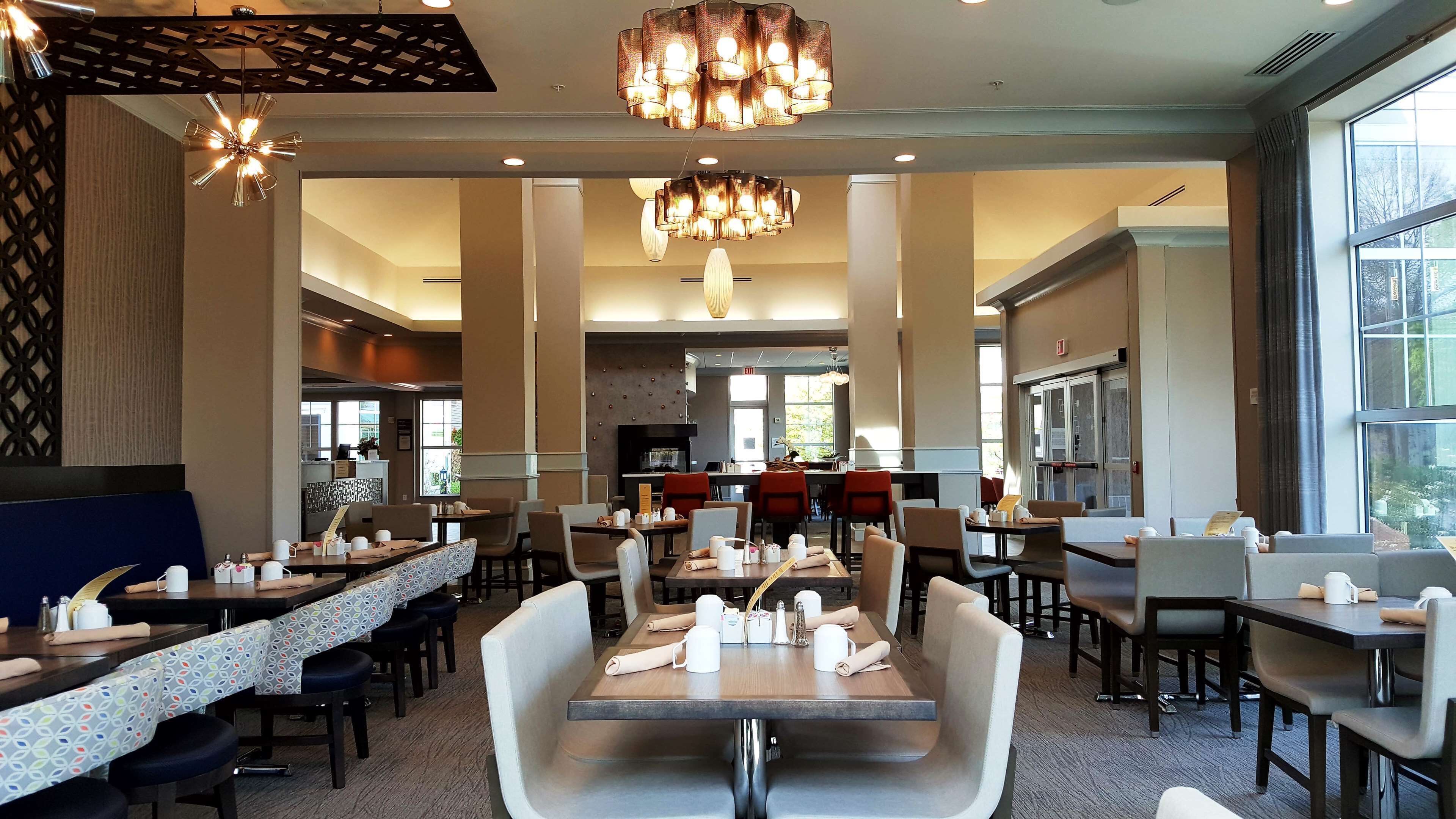 Un restaurante espacioso con techos altos, modernos candelabros y diversas opciones de asientos, incluyendo mesas y cabinas.