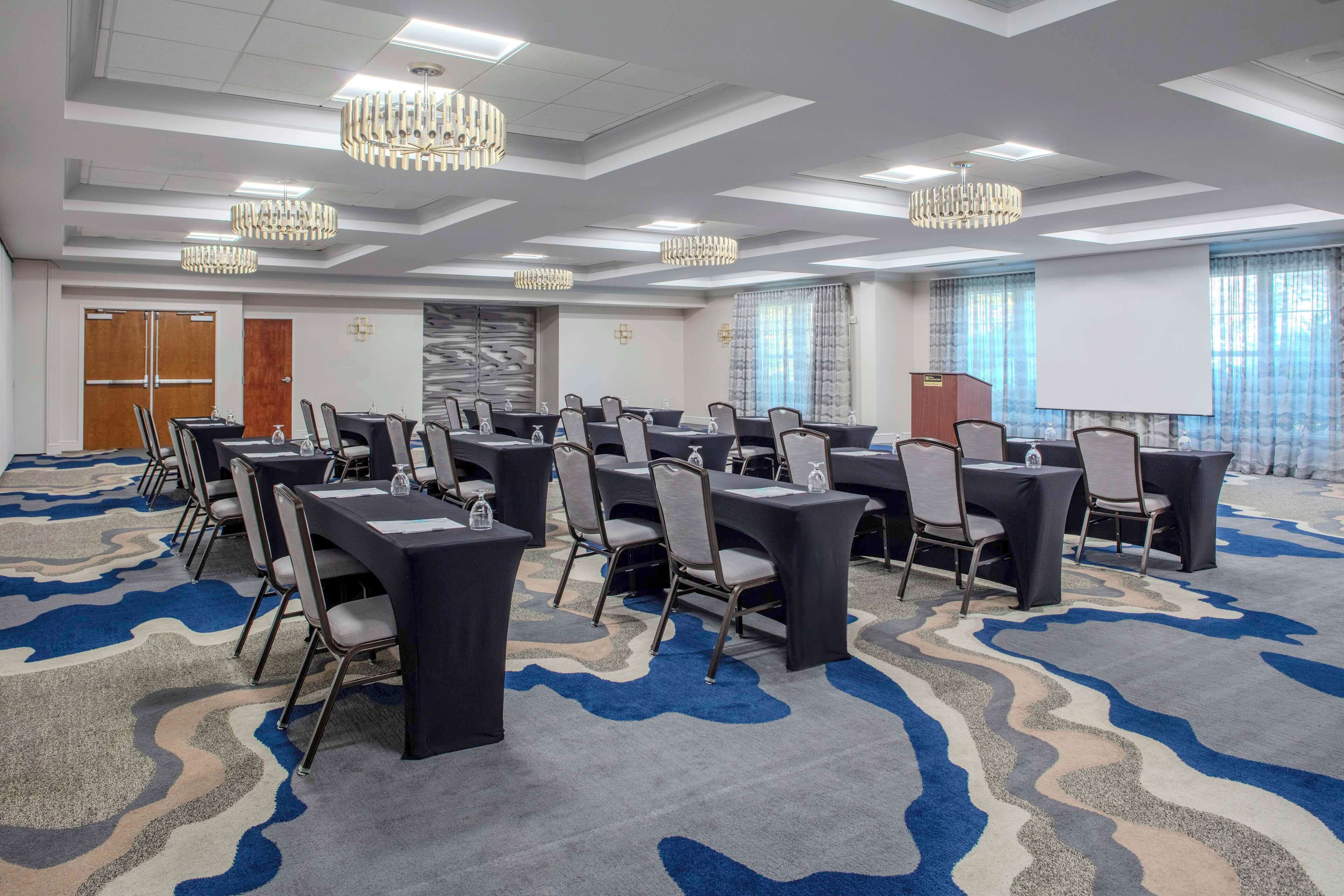 A conference room with multiple tables and chairs, a podium, and a large screen.