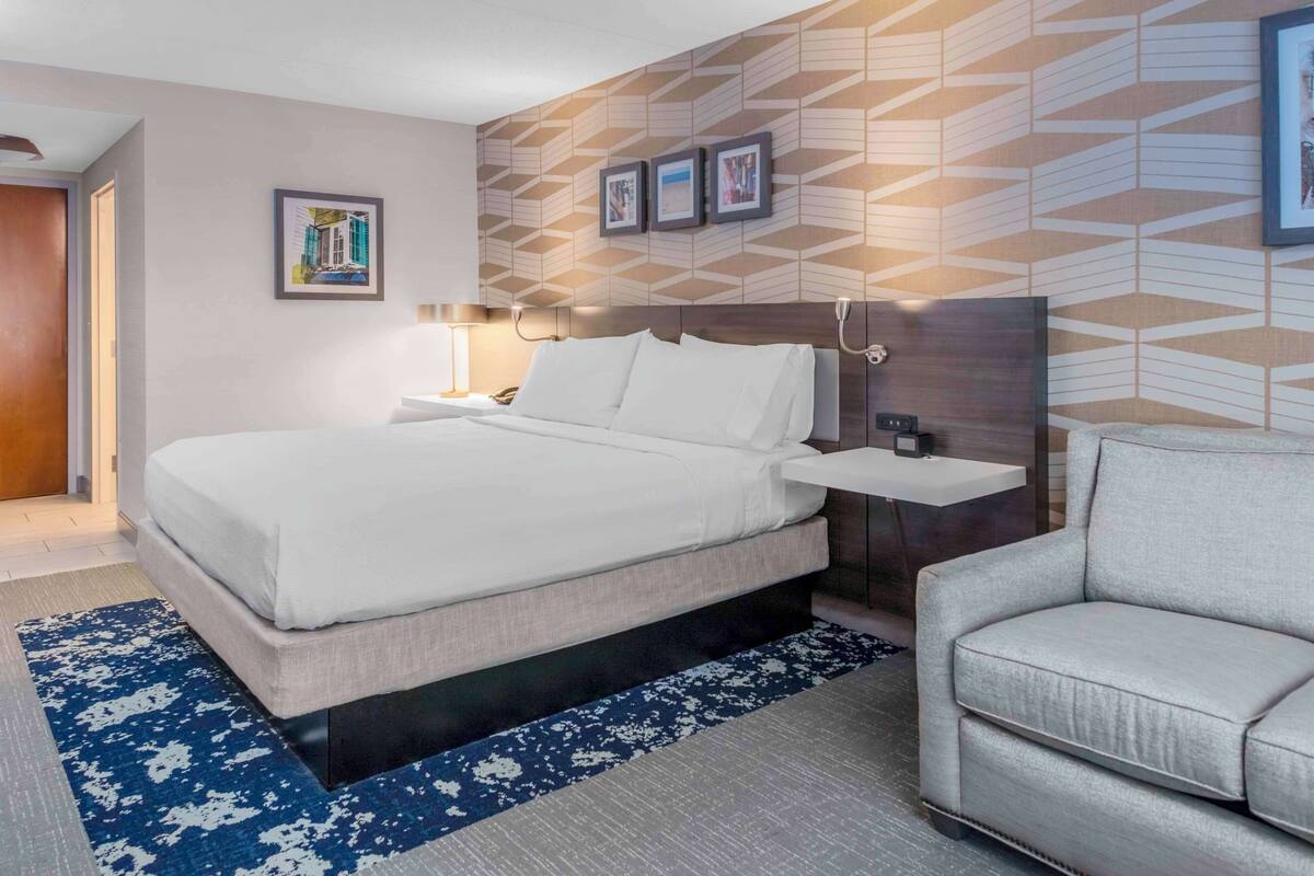 A hotel room with a bed, bedside table, lamp, and a sofa.