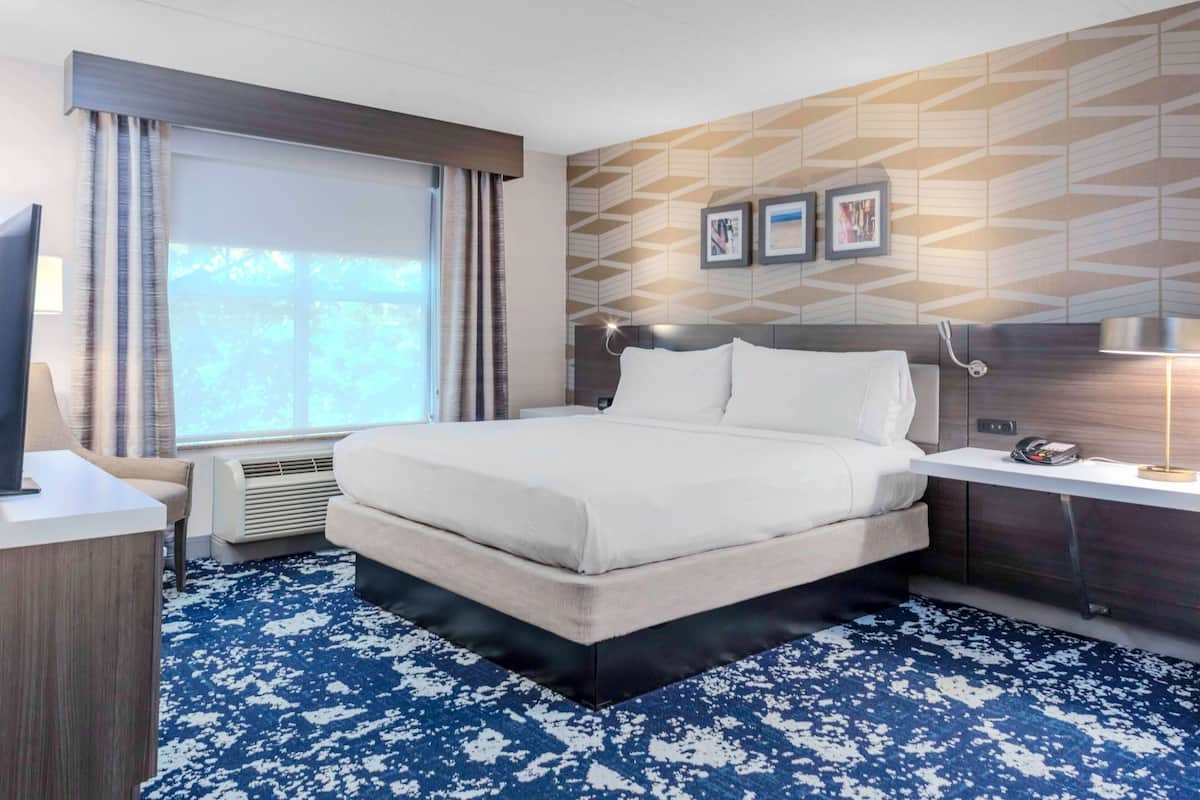 A hotel room with a large bed, a desk with a chair, a TV, and a window with curtains.