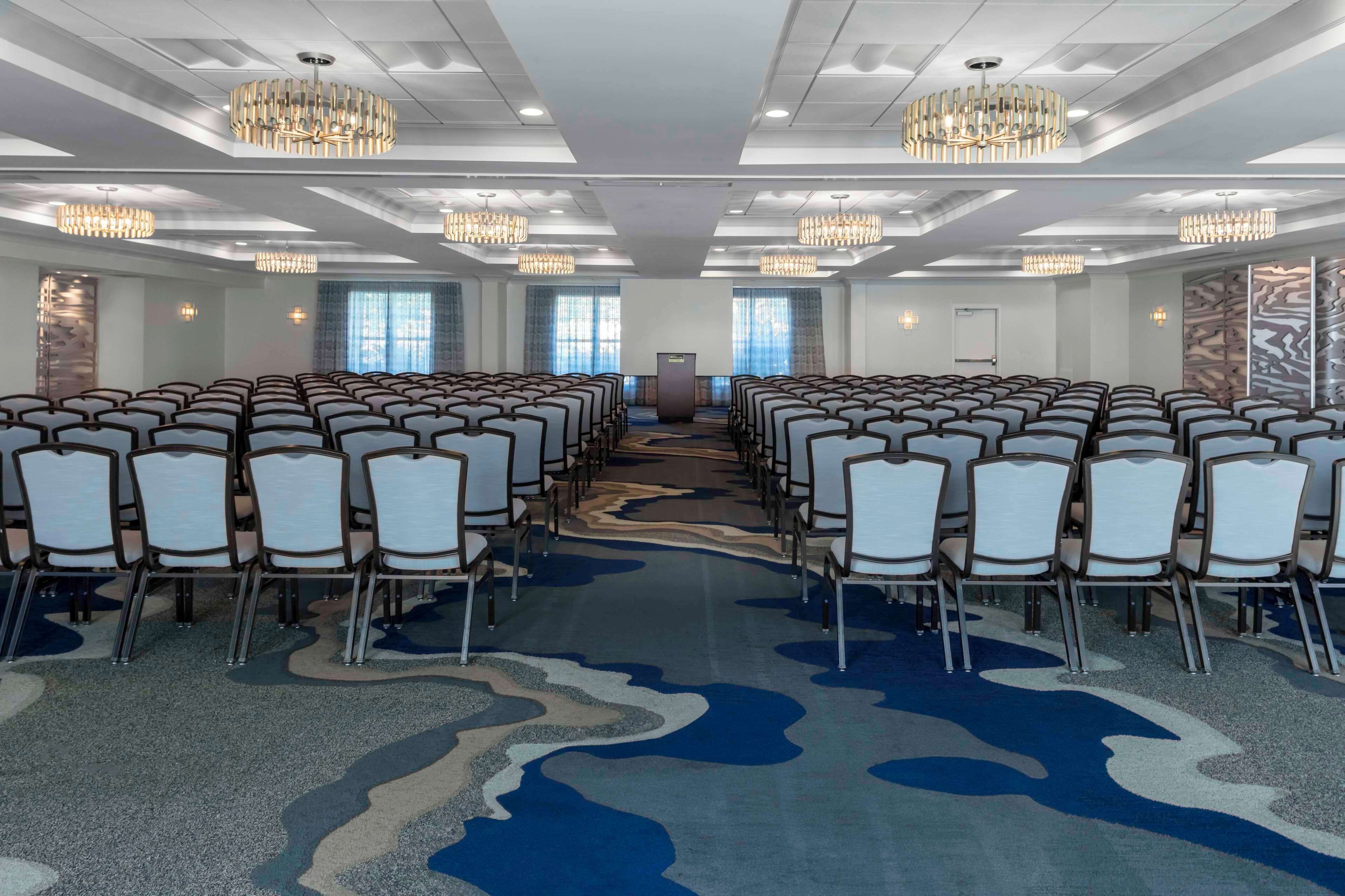 A conference room with rows of chairs, chandeliers, and a patterned carpet.