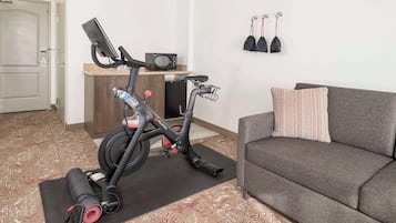 A compact living space with a stationary bike, a small kitchenette, and a grey sofa.