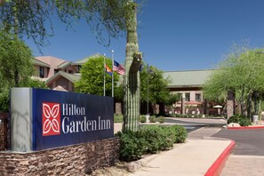 A Hilton Garden Inn sign with a clear view of the building's entrance, flagpoles, and surrounding landscaping. - Hilton Garden Inn Scottsdale North/Perimeter Center (Scottsdale)