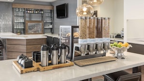 Et stilfuldt barområde med kaffestation, drikkevareautomater og en skål med frugt.