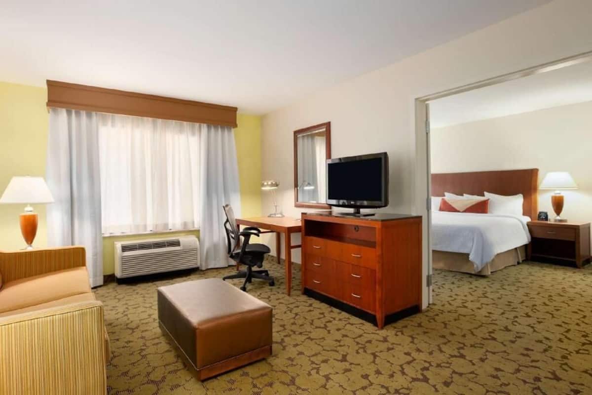 Habitación de hotel con cama, escritorio con computadora, televisor, sillón y lámpara.
