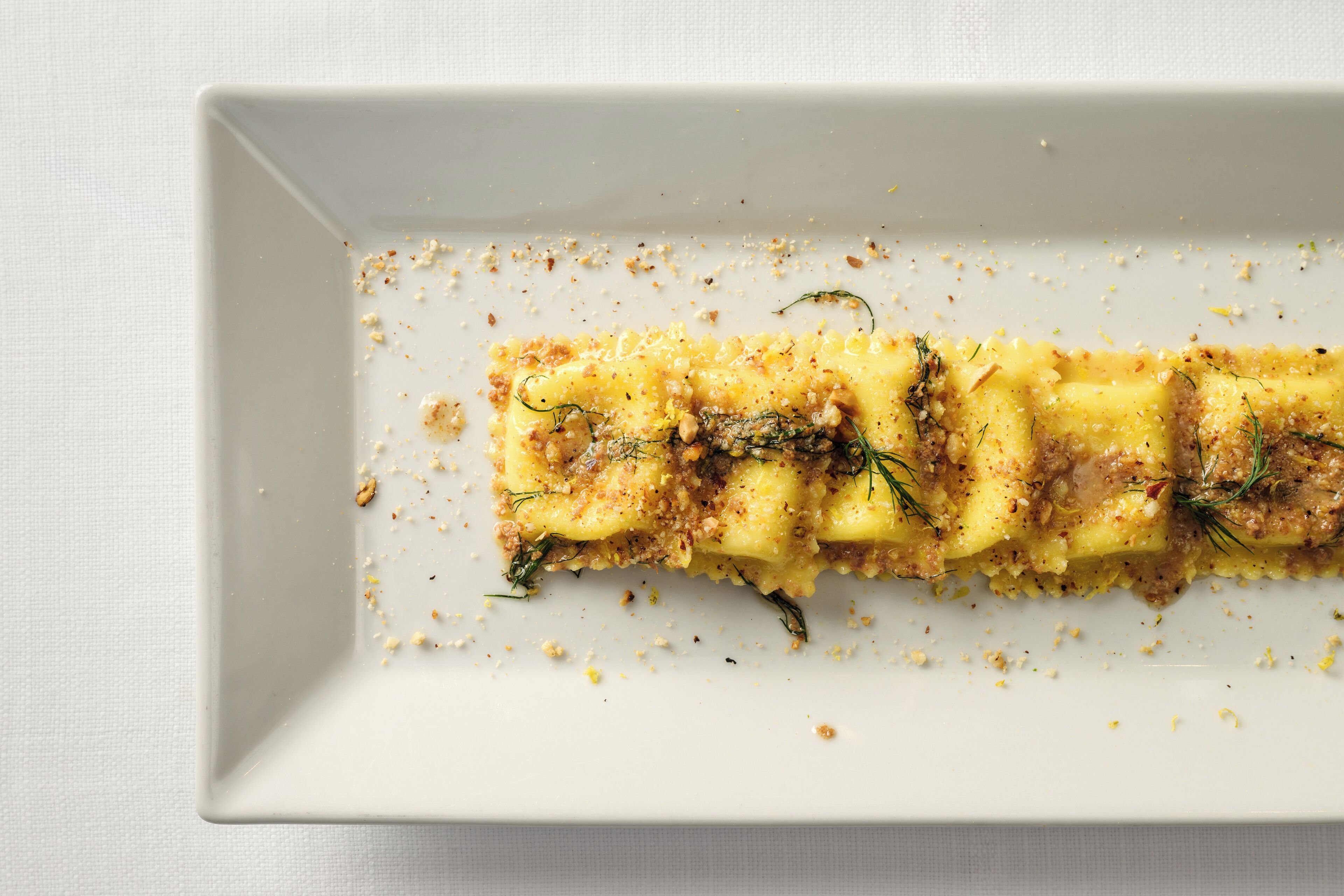 A rectangular white plate with a food item, possibly a dessert, garnished with herbs and crumbs.