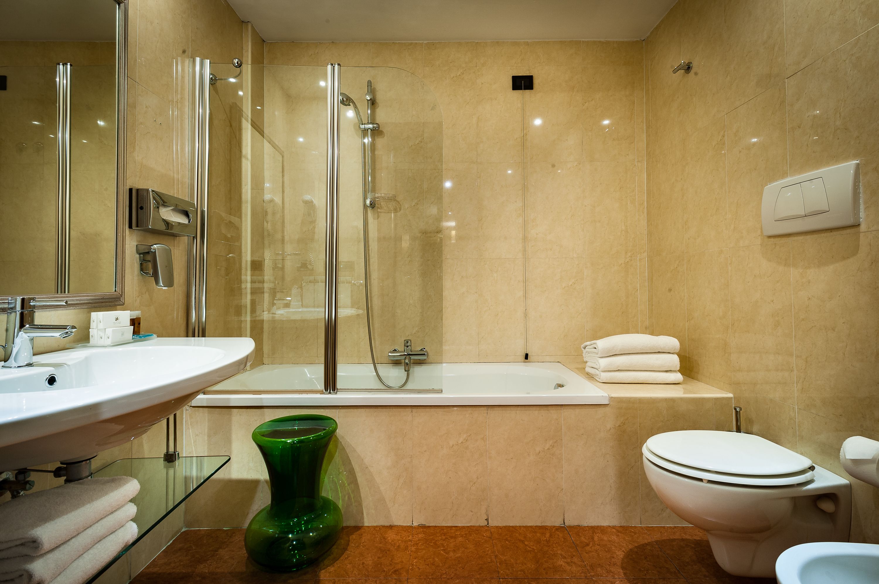 A modern bathroom with a glass-enclosed shower, a white bathtub, and a toilet.