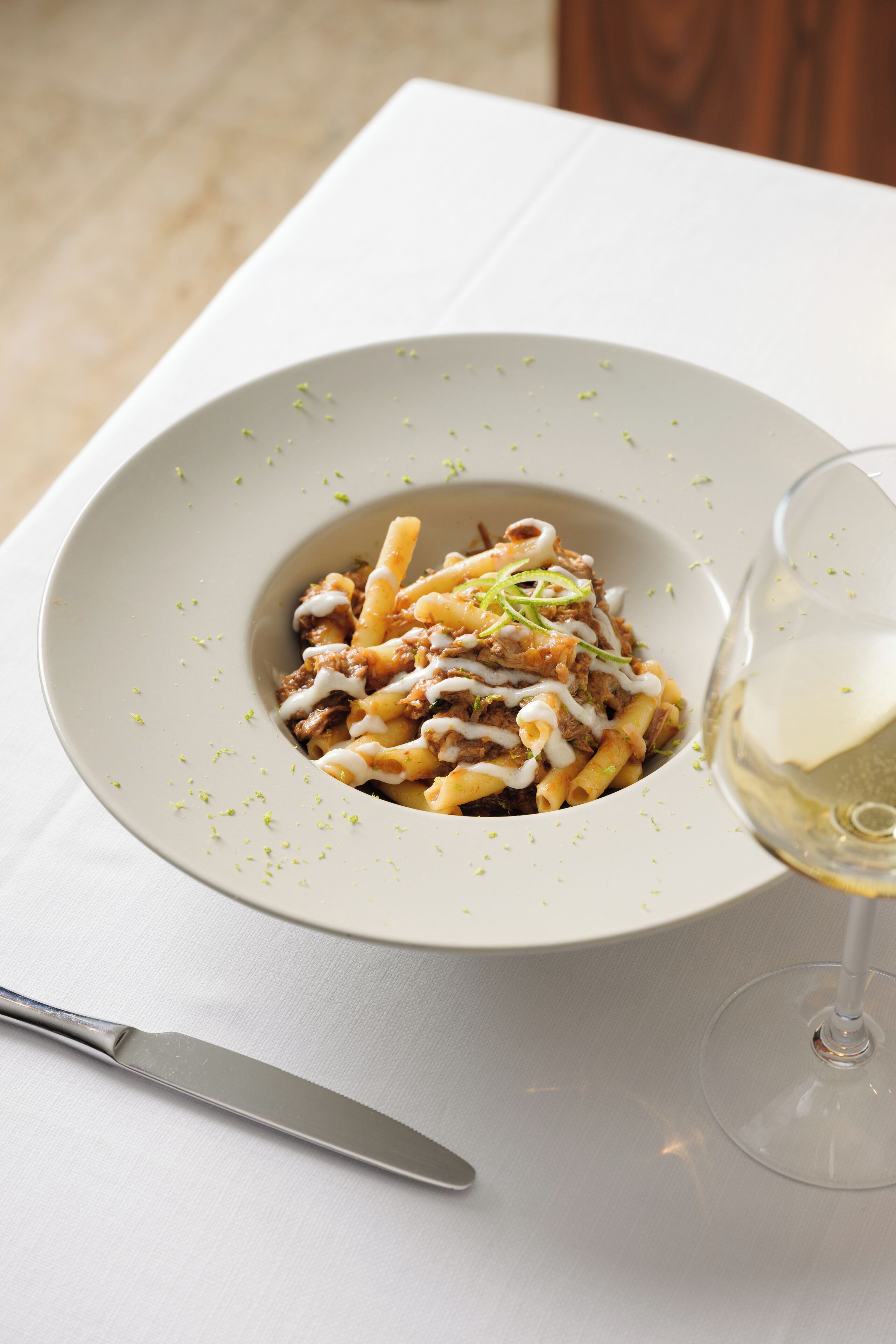 Eine Pasta-Zubereitung mit einem Glas Weißwein auf einem Tisch.
