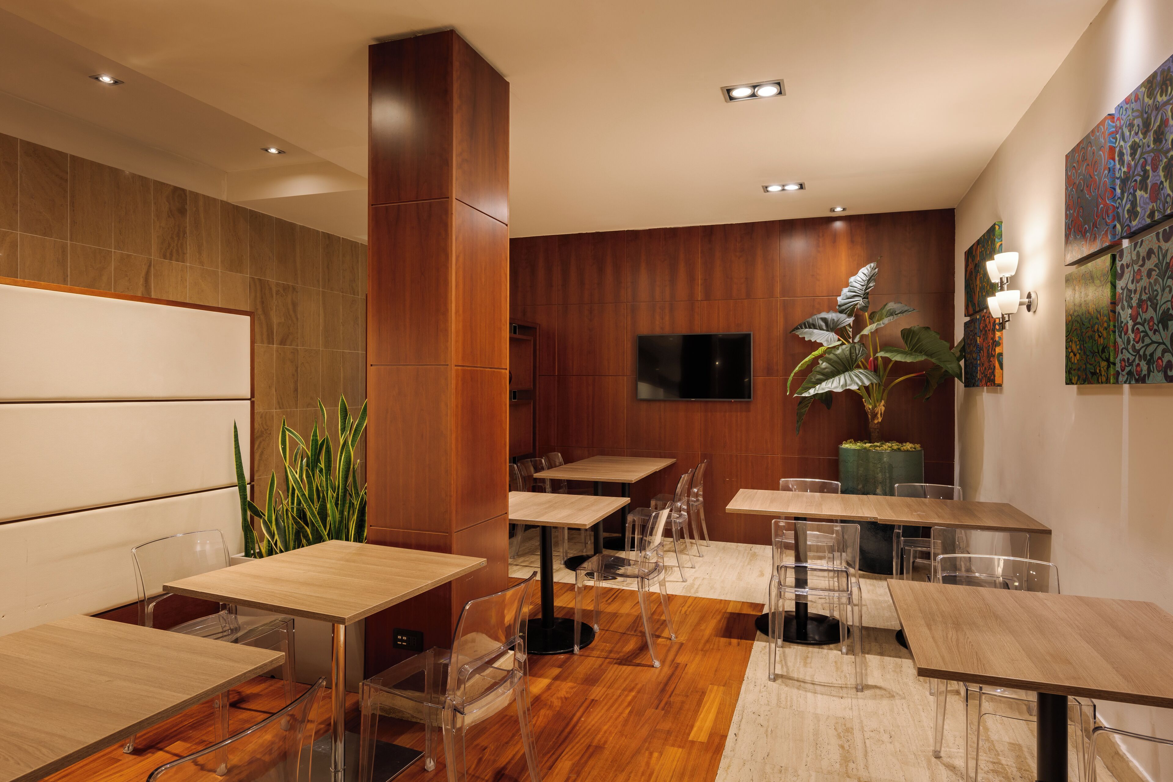A modern restaurant with wooden flooring, clear glass chairs, and a large potted plant.