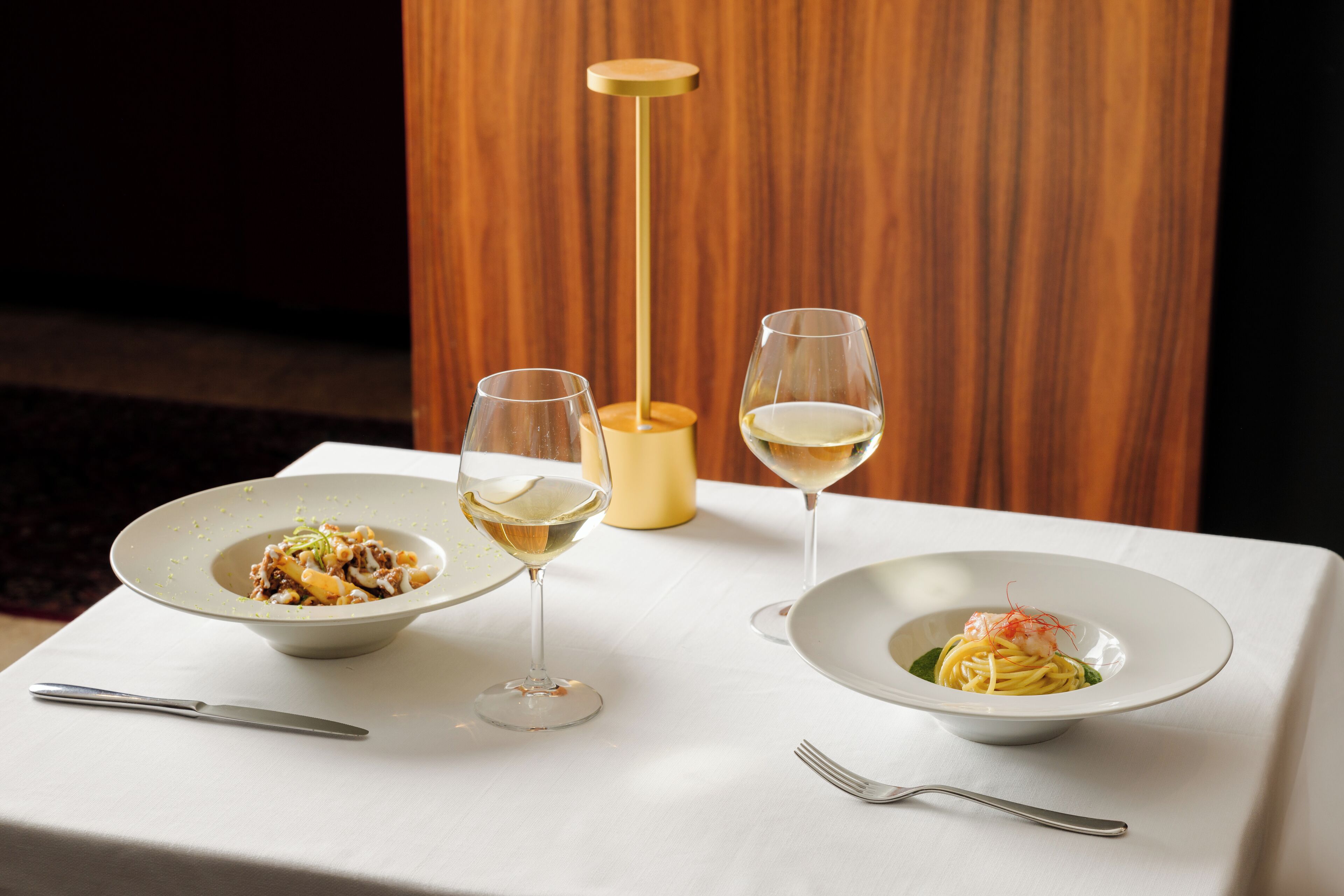 Una mesa con dos platos de pasta y dos copas de vino.