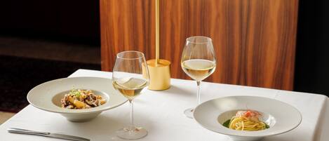 A table with two plates of pasta and two wine glasses.