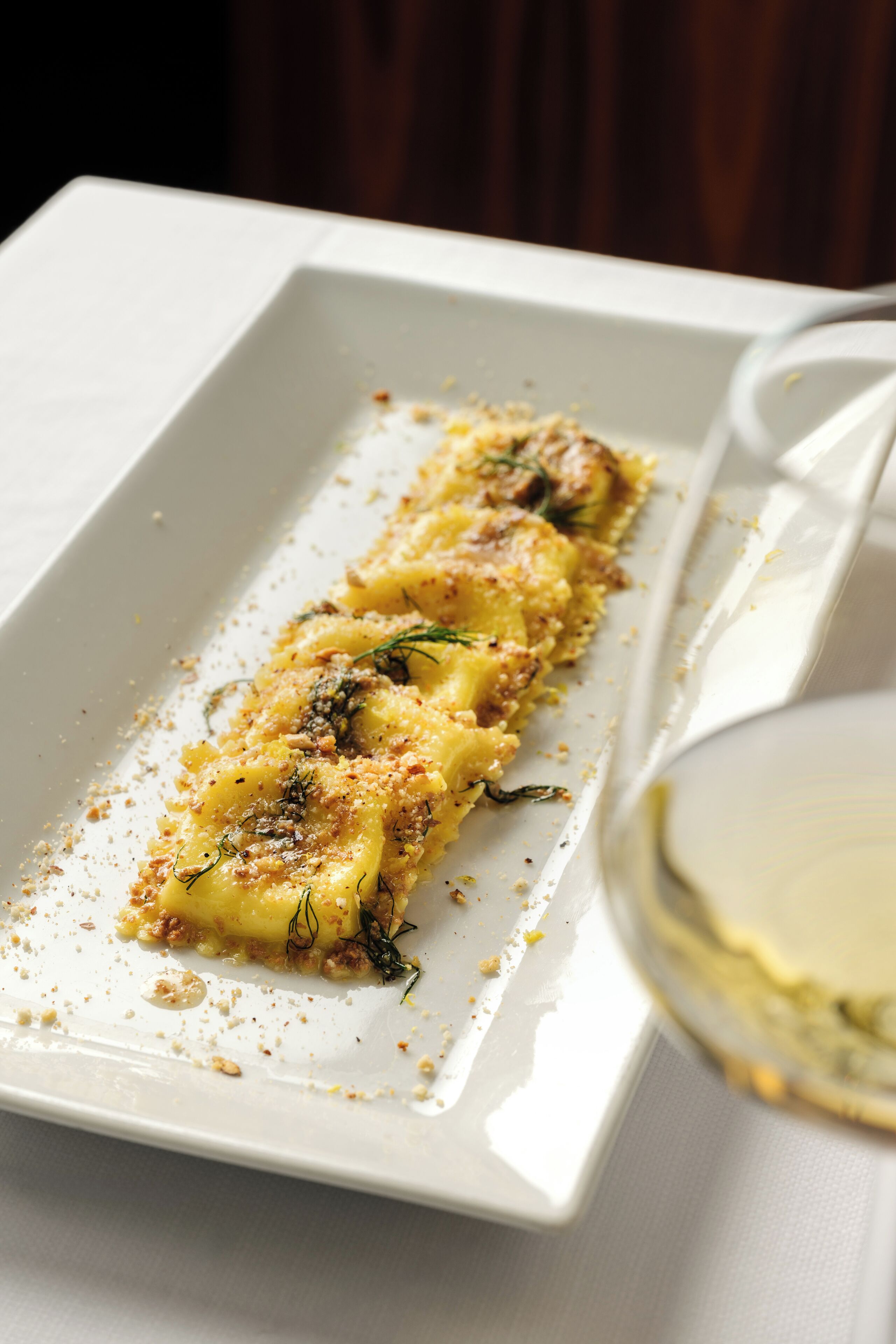 A rectangular white plate with a food item, possibly a pastry, garnished with herbs and crumbs.