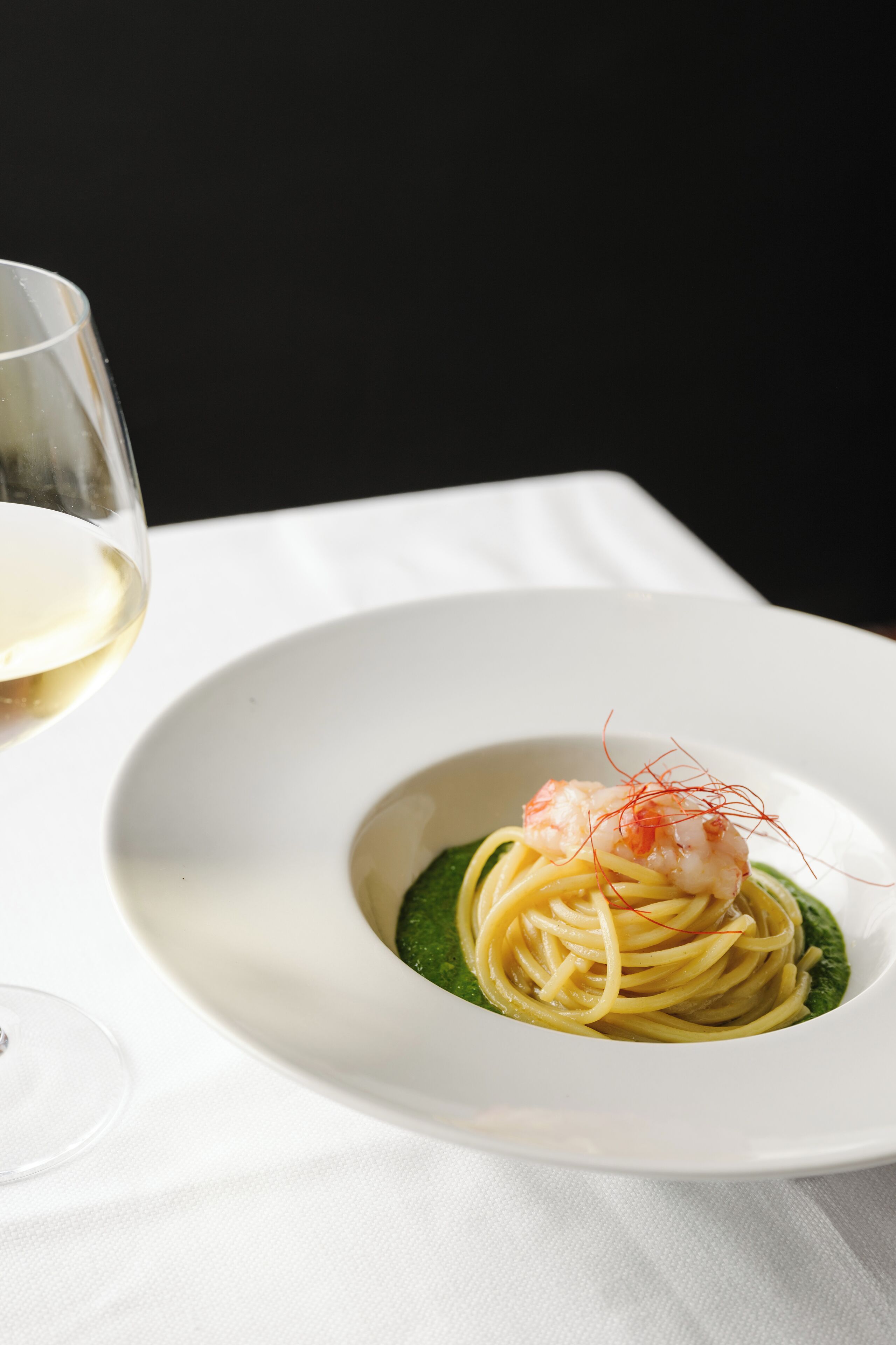 A white plate with pasta and a shrimp garnish on a white tablecloth.
