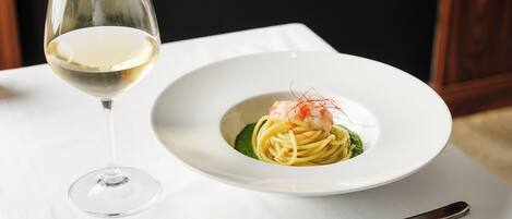 A plate of pasta with shrimp and a glass of white wine on a table.