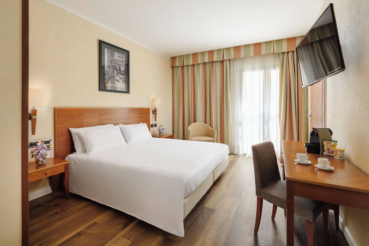 Une chambre d’hôtel avec un grand lit, un bureau avec une machine à café, une chaise et un téléviseur fixé au mur.