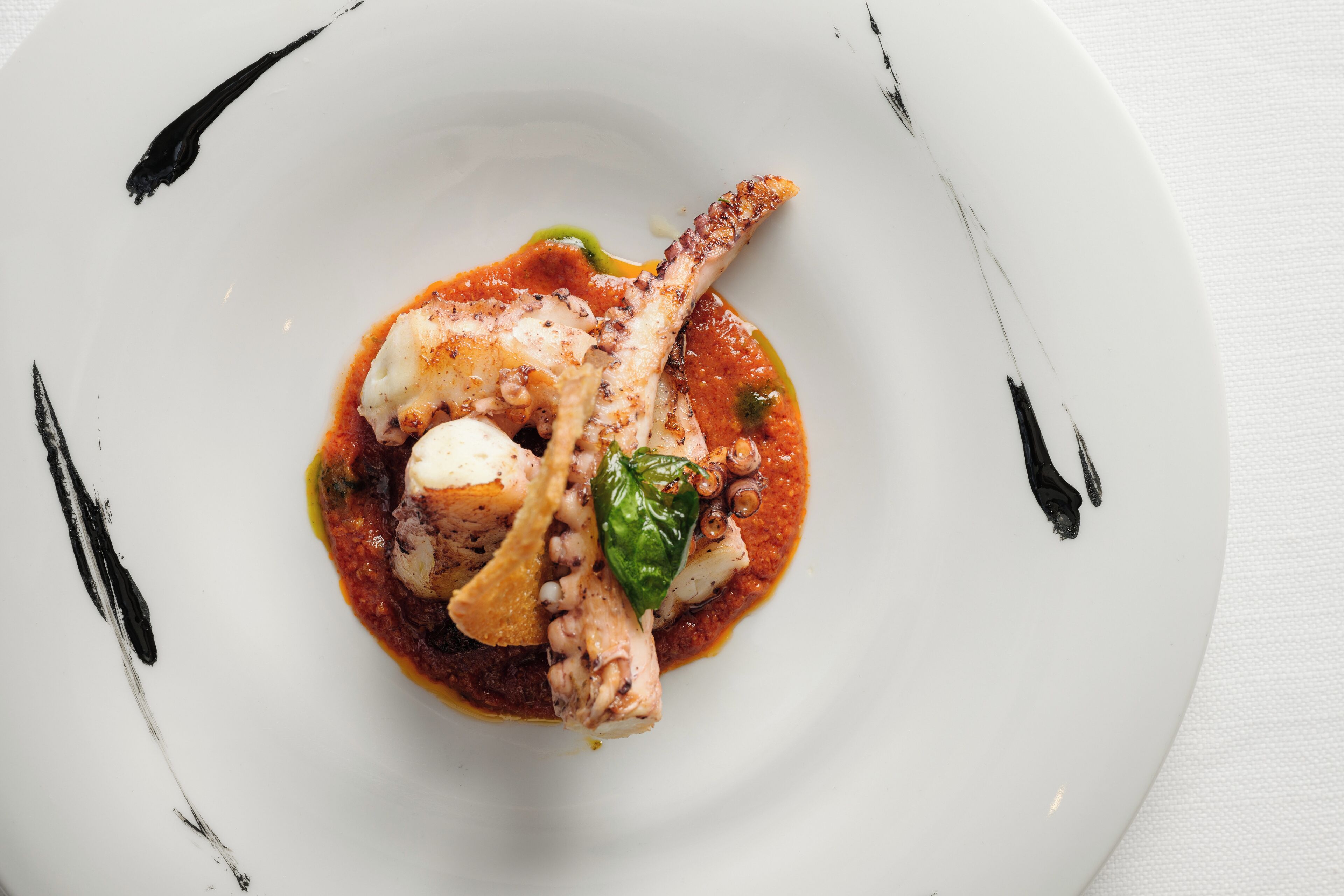 Un plat blanc amb un plat de pop, una fulla verda i una salsa vermella.