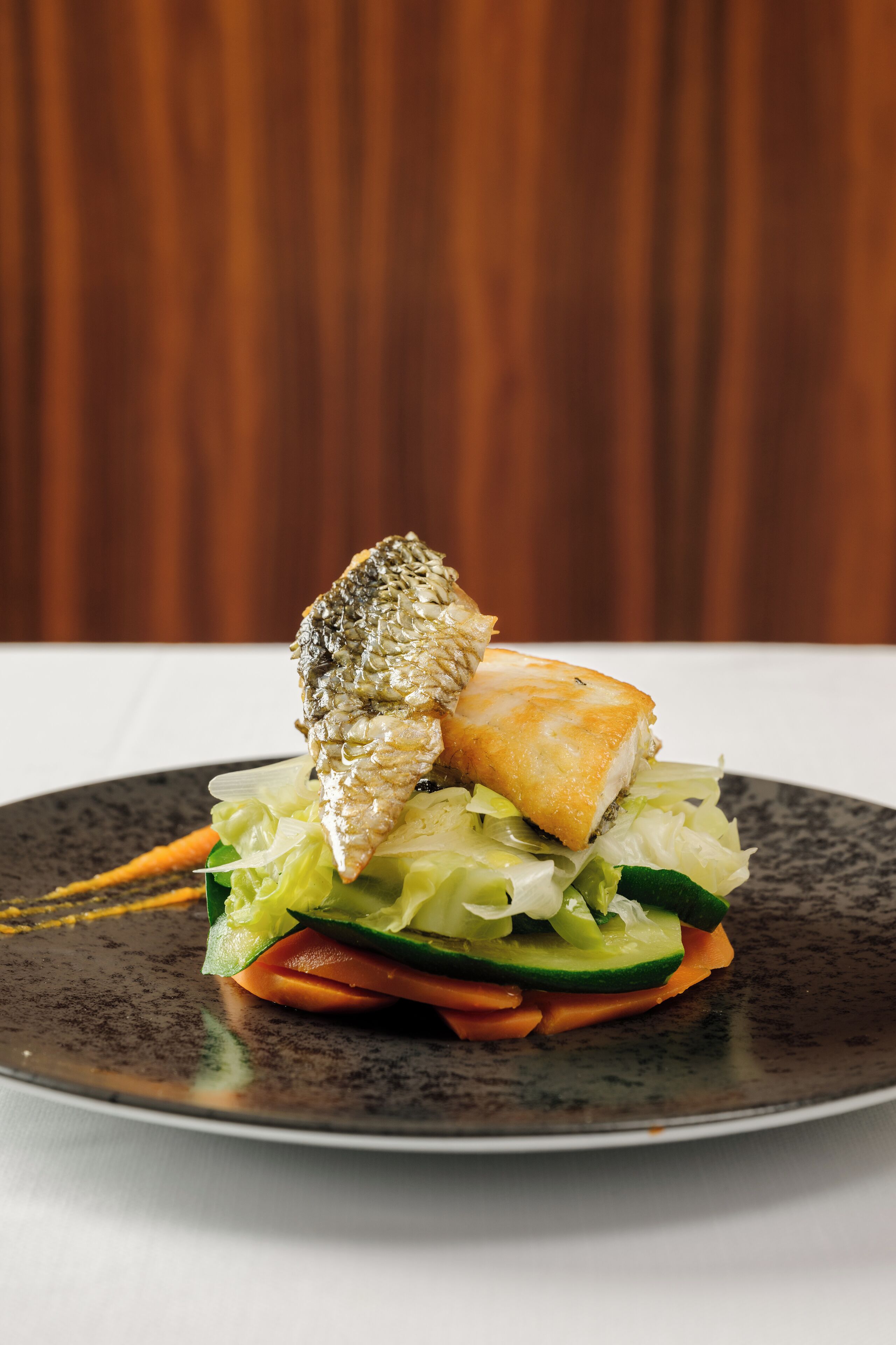 A plate with a fish, a piece of bread, and vegetables.