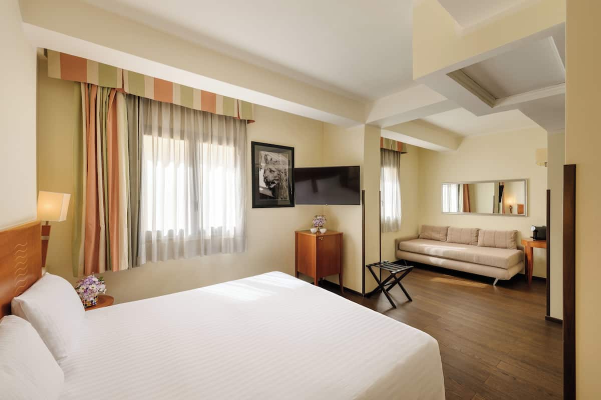 Une chambre d’hôtel avec un grand lit, un canapé, une télévision et un miroir.