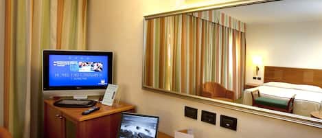 A hotel room with a desk, a laptop, a television, a coffee maker, and a bed.
