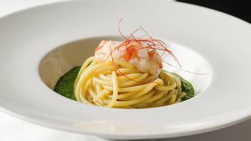 A white plate with a seafood dish, possibly pasta, garnished with red strands, on a white tablecloth.
