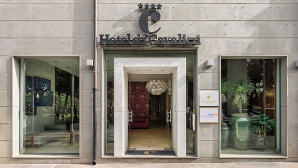 Der Eingang des Hotels da Cavalic, mit einer modernen Fassade, großen Glasfenstern und einladend gestaltetem Innenraum.
